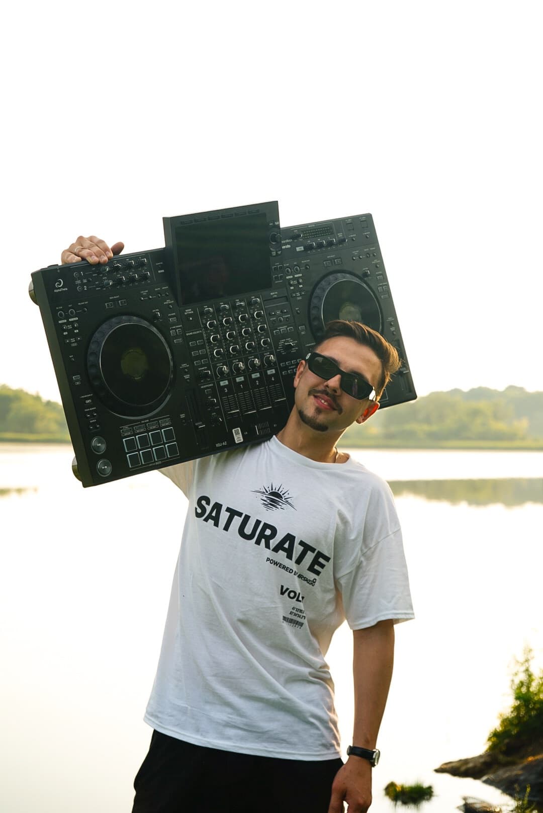 ARSKGG, Chicago DJ and producer, holding a DJ controller on his shoulder by the water